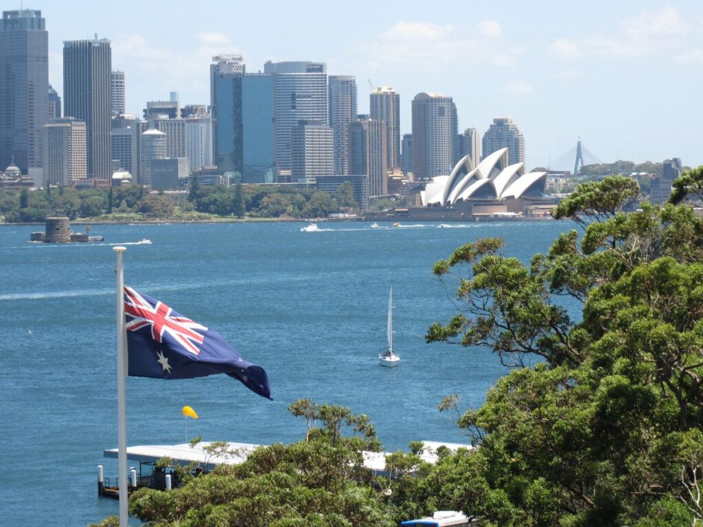 Harbour skyline with a national flag overlooking a modern city, symbolizing skilled migration opportunities and international career pathways in New Zealand.